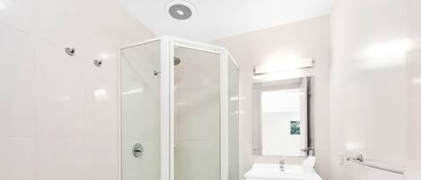 Une salle de bain moderne avec une douche à parois de verre, un lavabo blanc et un miroir au-dessus.