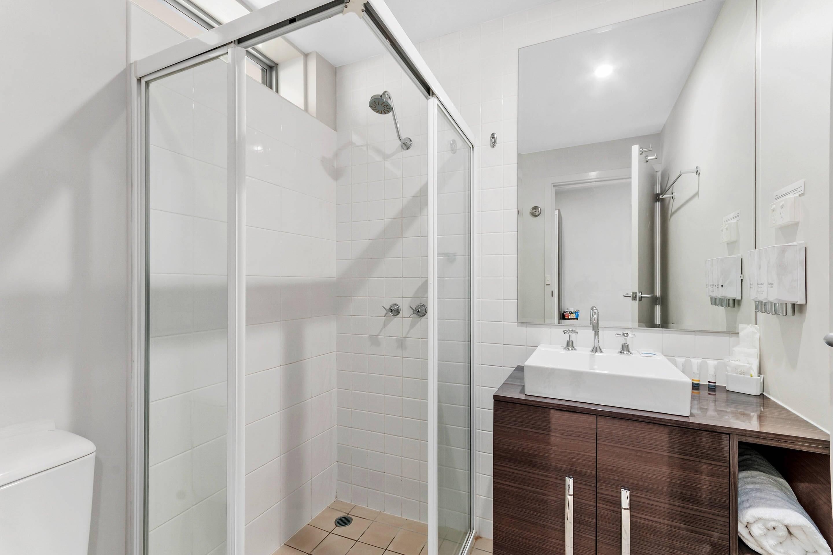 A modern bathroom with a glass-enclosed shower, a white sink, and a wooden vanity.