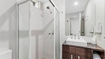 A modern bathroom with a glass-enclosed shower, a white sink, and a wooden vanity.