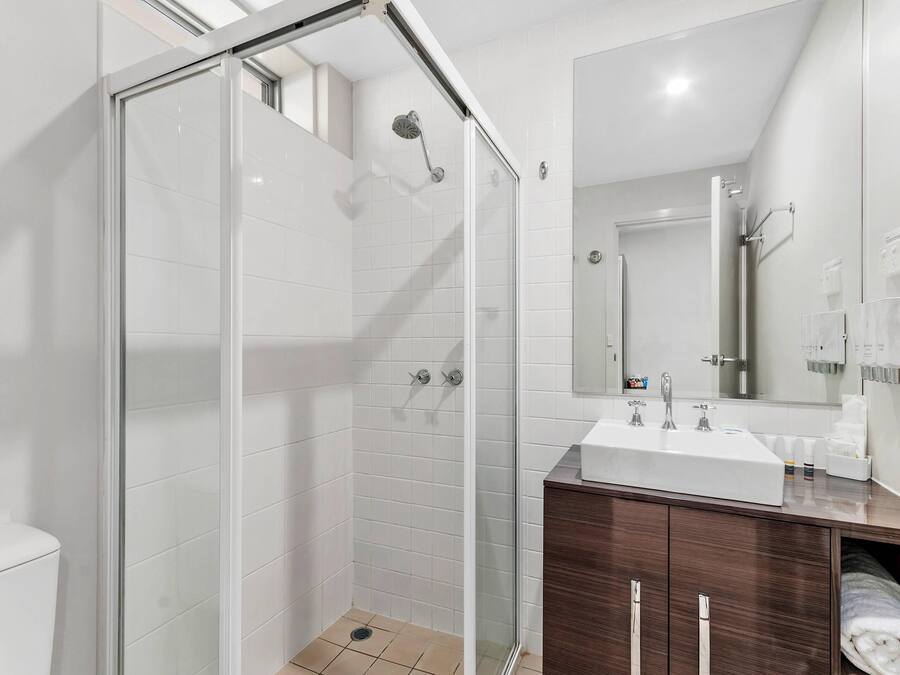 A modern bathroom with a glass-enclosed shower, a white sink, and a wooden vanity.
