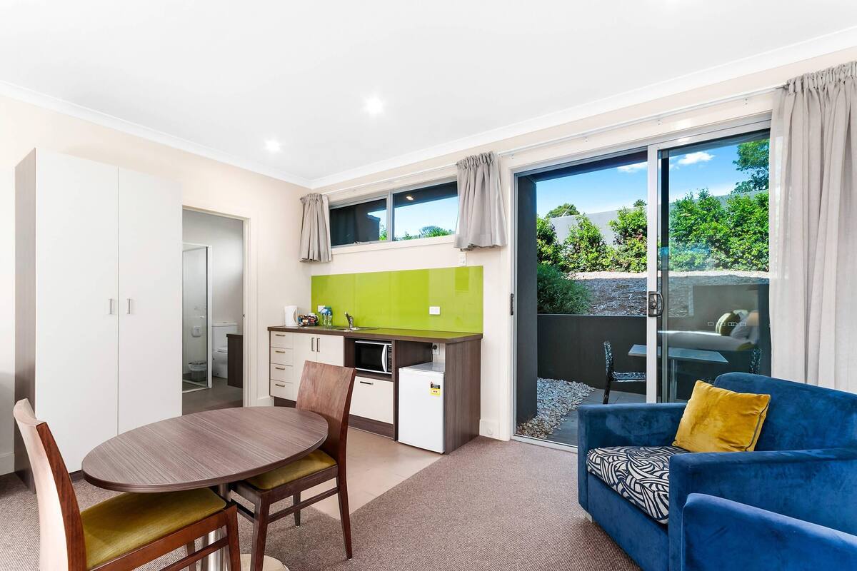 A compact living space with a dining table, chairs, a kitchenette, a sofa, and a sliding glass door leading to an outdoor area.