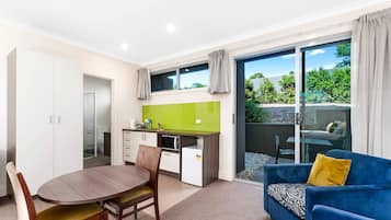 A compact living space with a dining table, chairs, a kitchenette, a sofa, and a sliding glass door leading to an outdoor area.