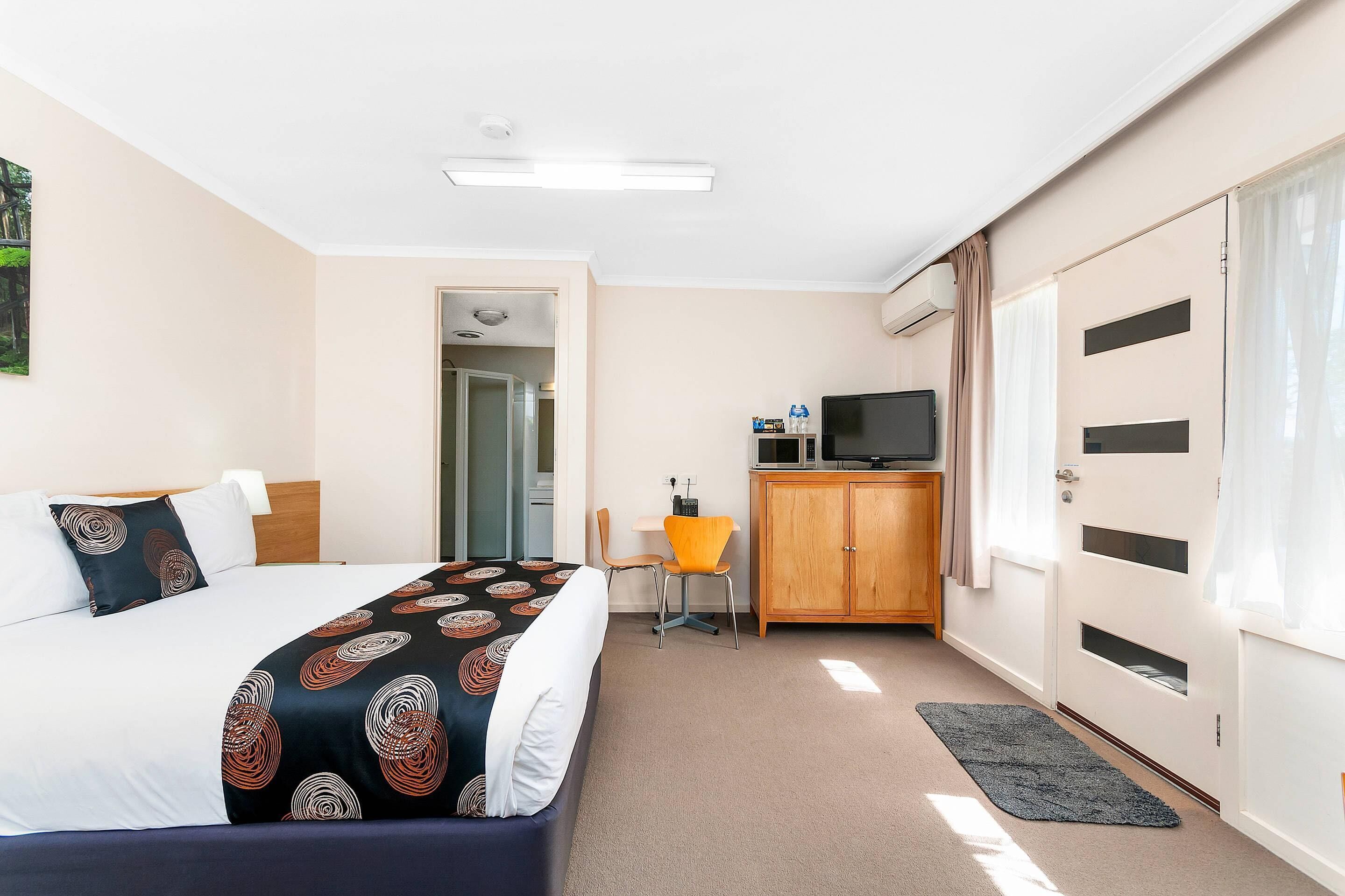 A hotel room with a bed, a desk, a TV, and a wardrobe.