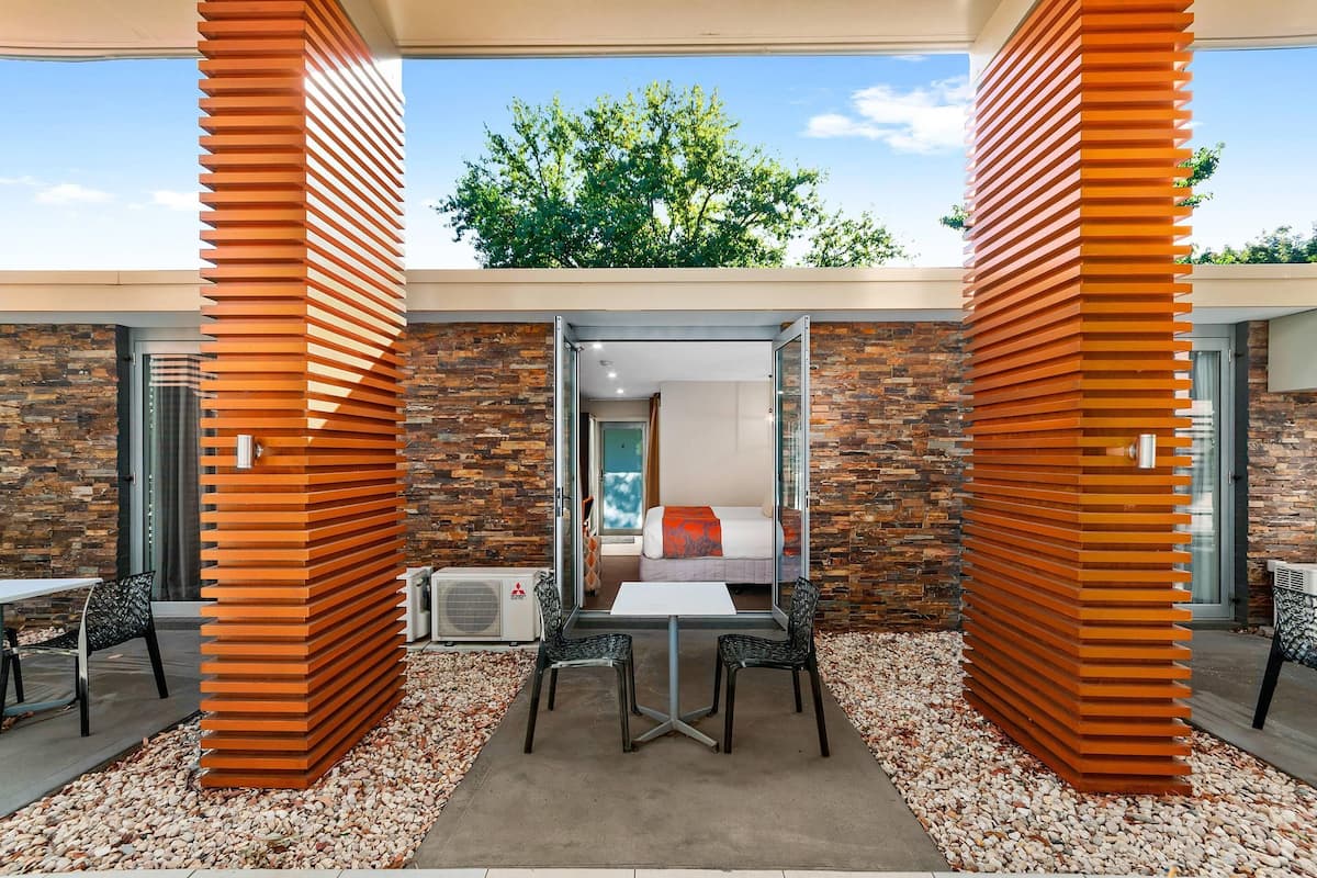 A modern hotel room with a stone wall, a bed with a red blanket, and a view of a tree.