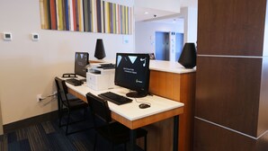 A reception desk with two computer monitors, a keyboard, and a mouse. There are two chairs, a wall-mounted clock, and a colorful striped artwork above the desk. - Holiday Inn Express & Suites Houston IAH - Beltway 8 by IHG (Houston)