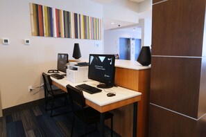 A reception desk with two computer monitors, a keyboard, and a mouse. There are two chairs, a wall-mounted clock, and a colorful striped artwork above the desk. - Holiday Inn Express & Suites Houston IAH - Beltway 8 by IHG (Houston)