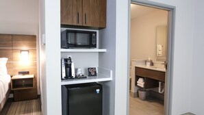 A compact hotel room with a bed, a small bedside table with a lamp, a microwave, a mini-fridge, and a coffee maker. - Holiday Inn Express & Suites Houston IAH - Beltway 8 by IHG (Houston)