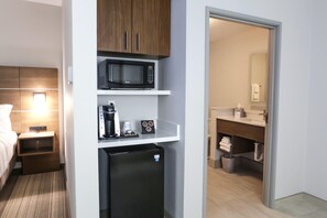 A compact hotel room with a bed, a small bedside table with a lamp, a microwave, a mini-fridge, and a coffee maker. - Holiday Inn Express & Suites Houston IAH - Beltway 8 by IHG (Houston)