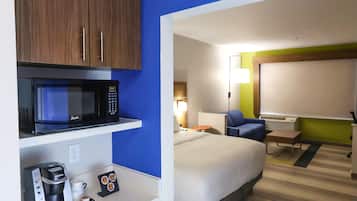 Una habitación de hotel con una cama, un escritorio con cafetera, microondas y televisión.