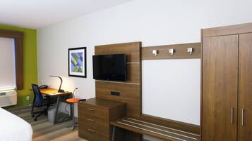 A hotel room with a bed, a desk with a chair, a television, a wardrobe, and a framed picture on the wall.