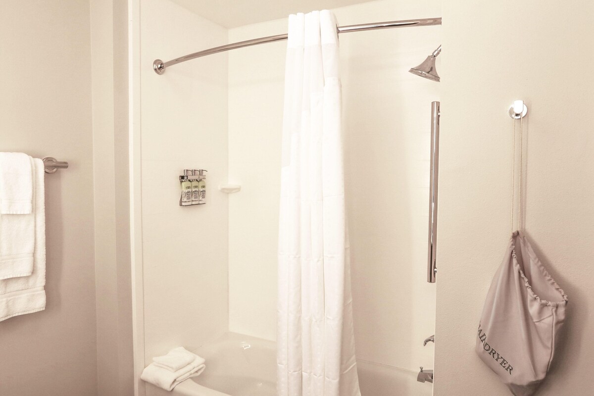 A shower with a glass door, a towel rack with folded towels, and a bag hanging on the wall.