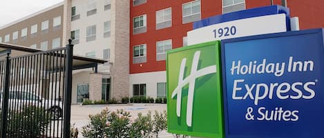 Edificio de Holiday Inn Express & Suites con diseño moderno, destacando un letrero grande con el número '1920' y una entrada protegida por una reja.