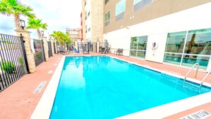 A rectangular pool with a 4ft 6in width marking, surrounded by a tiled deck, palm trees, and a building with large windows. - Holiday Inn Express & Suites Houston IAH - Beltway 8 by IHG (Houston)