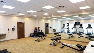 Un gimnasio con equipo de ejercicio, un muro de espejos y piso alfombrado.