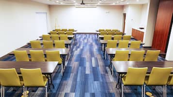 A conference room with rows of tables and chairs, a carpeted floor, and a whiteboard at the front.