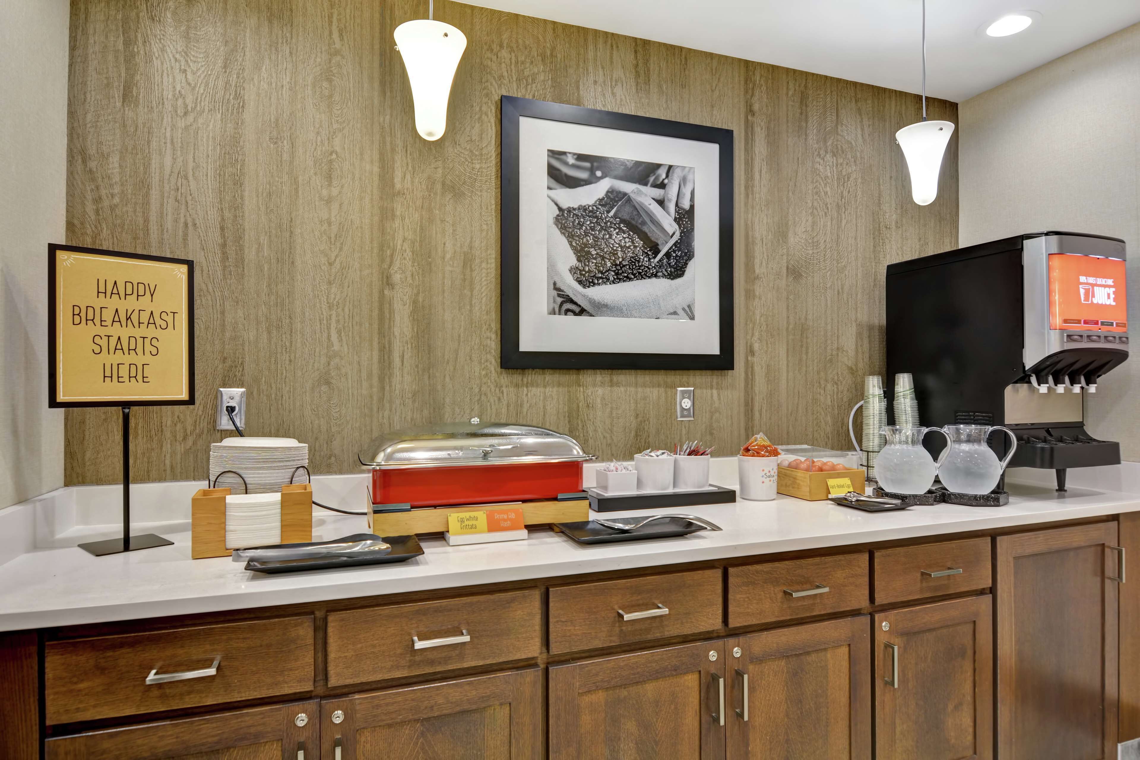 A breakfast bar with a sign that reads "HAPPY BREAKFAST STARTS HERE," a coffee machine, and a framed picture on the wall.