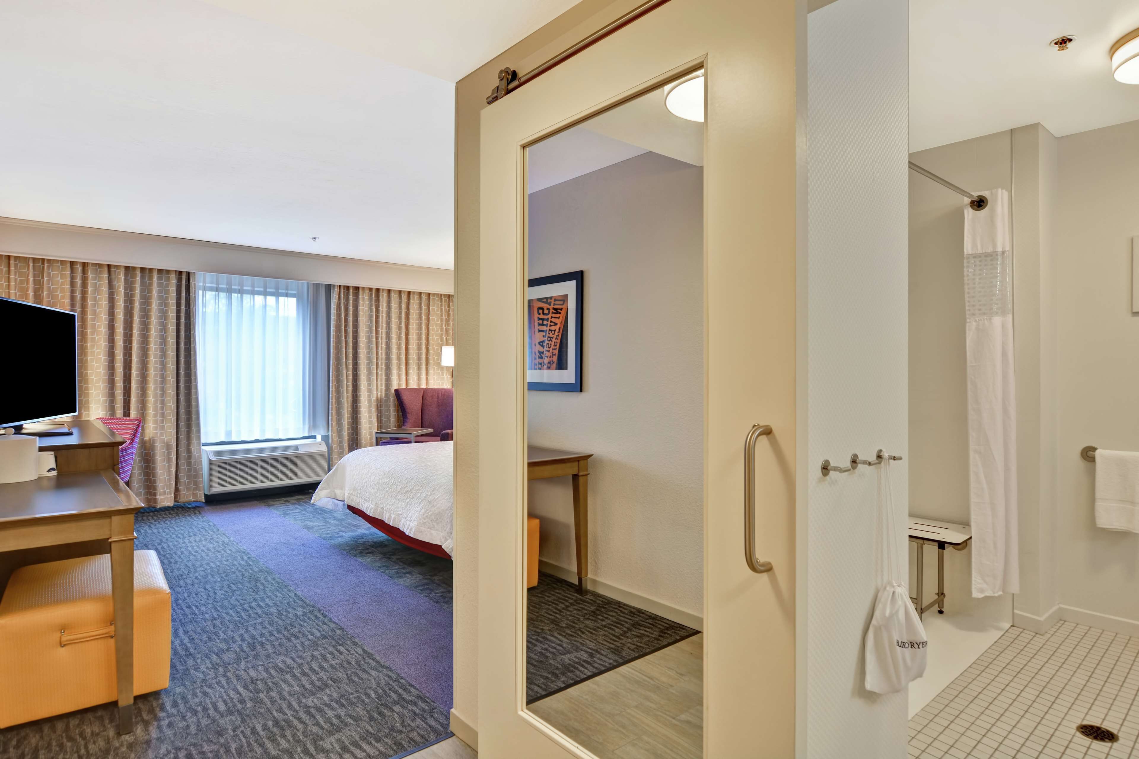 A hotel room with a bed, a desk, a television, a shower, and a bathroom with a towel rack.