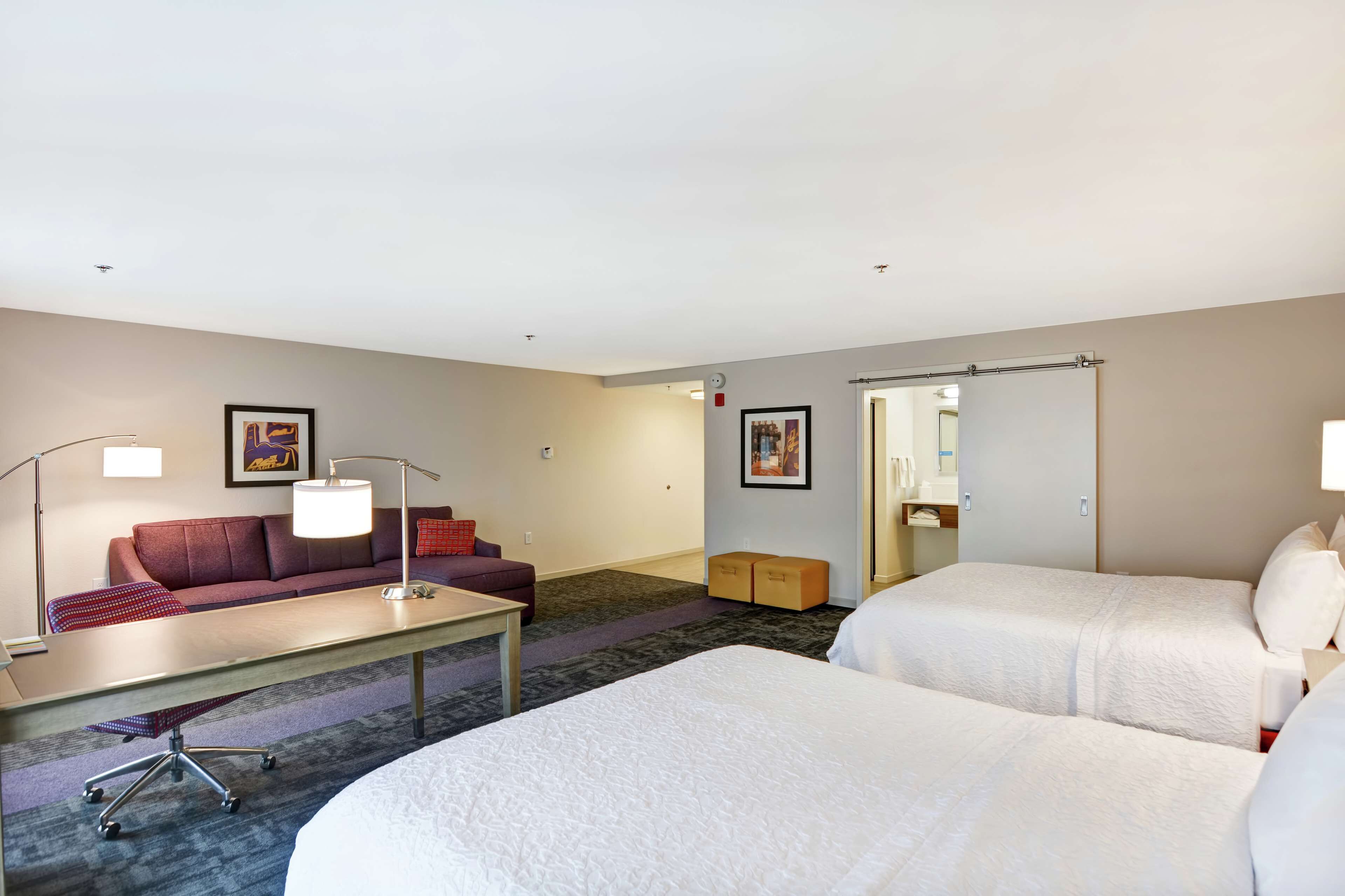 A hotel room with two beds, a desk, a sofa, and a carpeted floor.