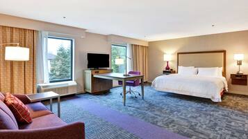 A hotel room with a bed, a desk with a computer, a TV, and a window with curtains.
