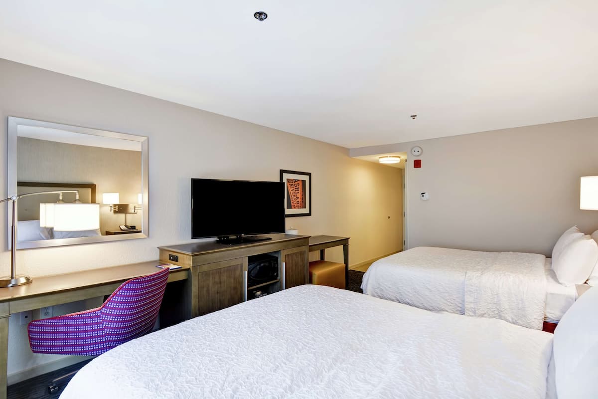 A hotel room with two beds, a desk with a television, a chair, and a mirror.