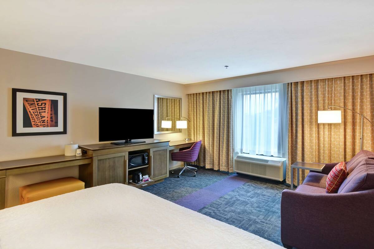 A hotel room with a bed, a desk with a computer, a television, a chair, and a couch.
