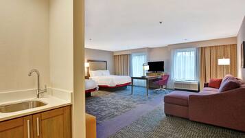 A hotel room with a bed, a desk, a couch, a TV, and a sink.