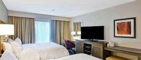 A hotel room with two beds, a desk with a television, a chair, and a framed picture on the wall.