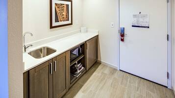A kitchen with a stainless steel sink, wooden cabinets, a white countertop, and a framed picture on the wall.