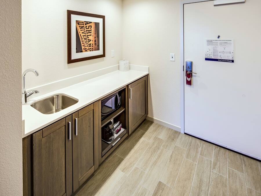 A kitchen with a stainless steel sink, wooden cabinets, a white countertop, and a framed picture on the wall.