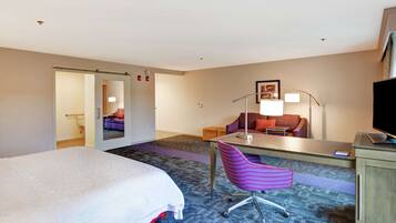 Una habitación de hotel con cama, escritorio y silla, sofá, televisor y lámpara.