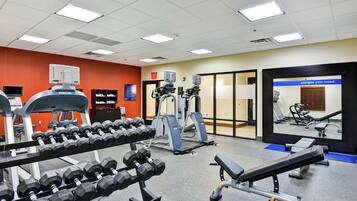 Une salle de sport équipée de divers appareils d’exercice, notamment des haltères, des machines de musculation et des bancs.