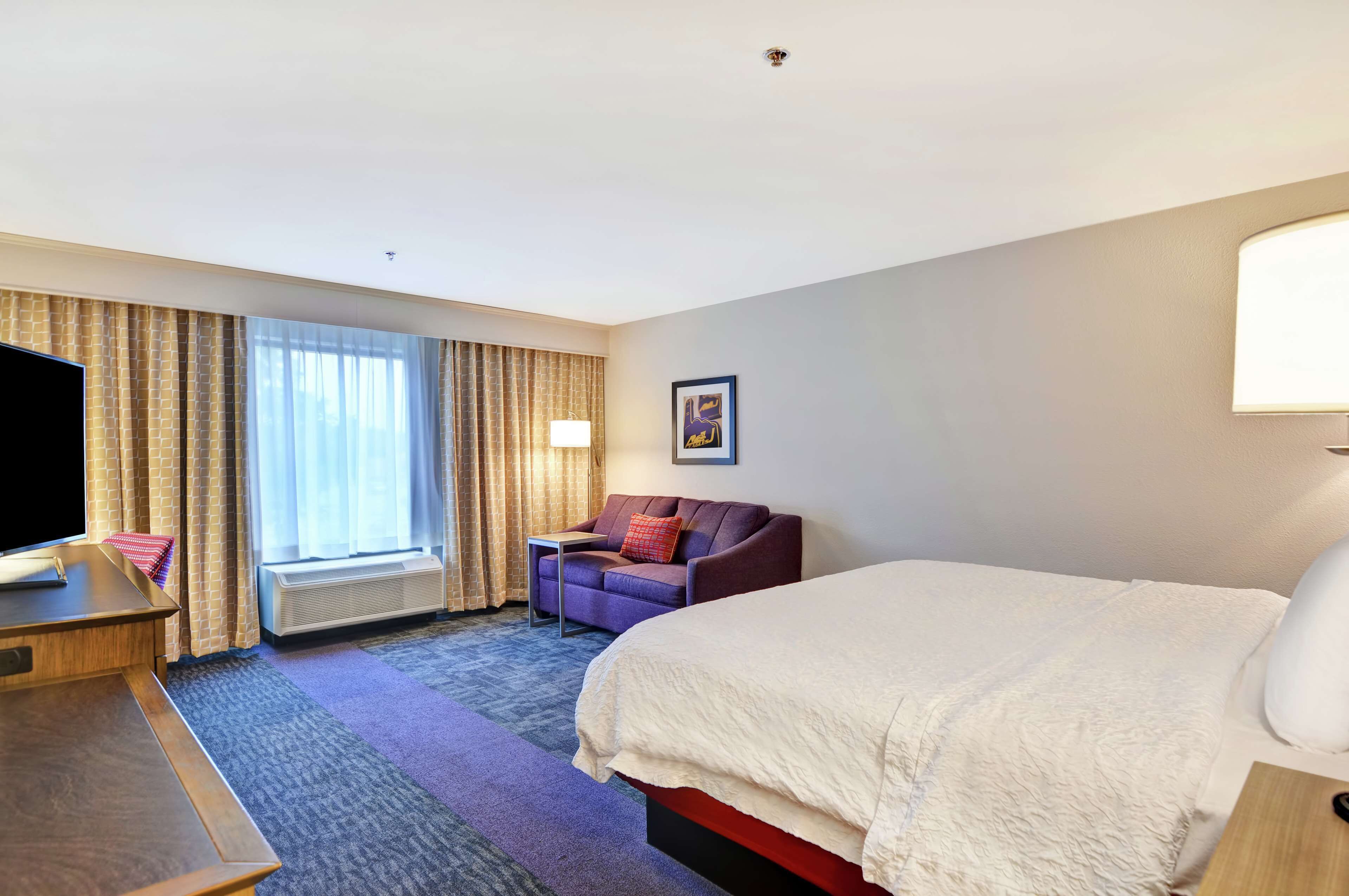 Een hotelkamer met een groot bed, een bureau met een flatscreen televisie, een bank en een raam met gordijnen.