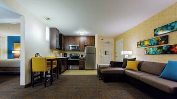 A hotel room with a kitchenette, a dining area, a sofa, and a bed.