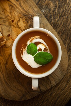 A white cup of coffee with foam and a green leaf on a wooden surface.