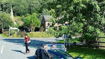 Une voiture décapotable verte, modèle ancien, est garée sur une route, et une personne marche à côté.