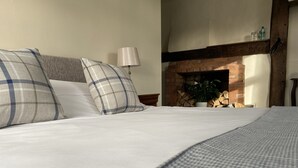 A neatly made bed with plaid pillows, a lamp, and a brick fireplace in the background. - The Talbot at Knightwick (Worcester)