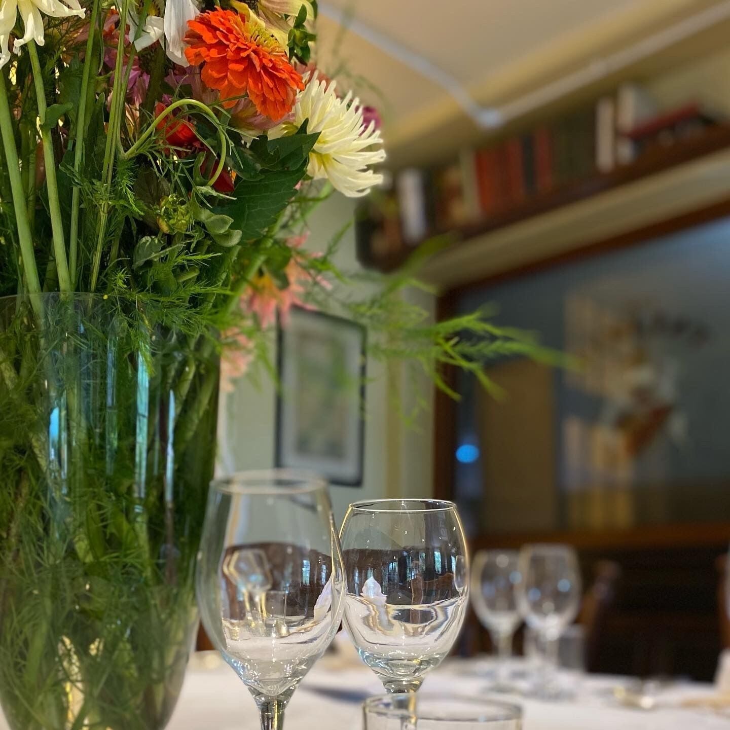 Una mesa con un florero de vidrio transparente que contiene un ramo de flores y dos copas de vino vacías.