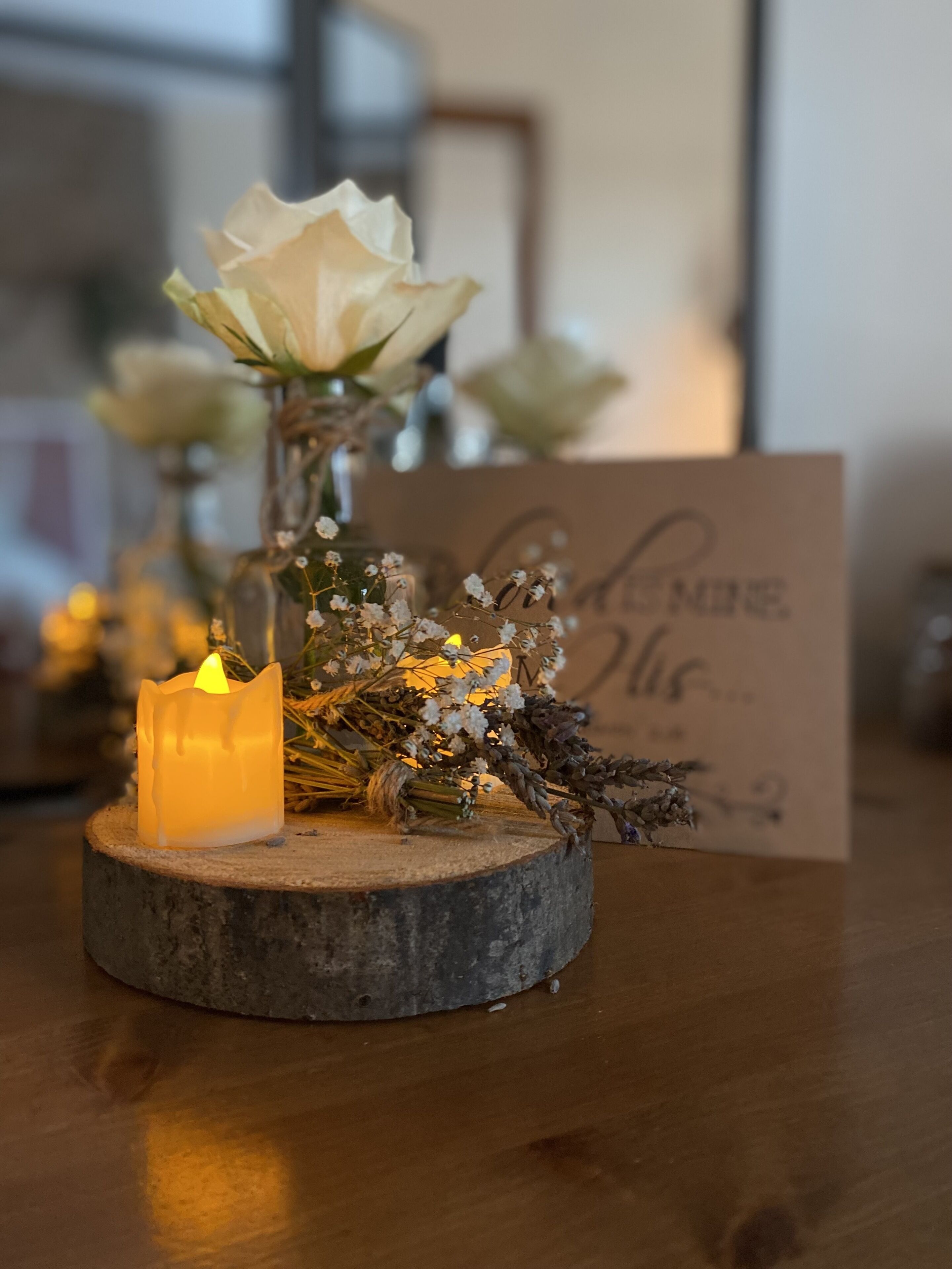 Una vela sobre un posavasos de madera, con un ramo de flores y una tarjeta.