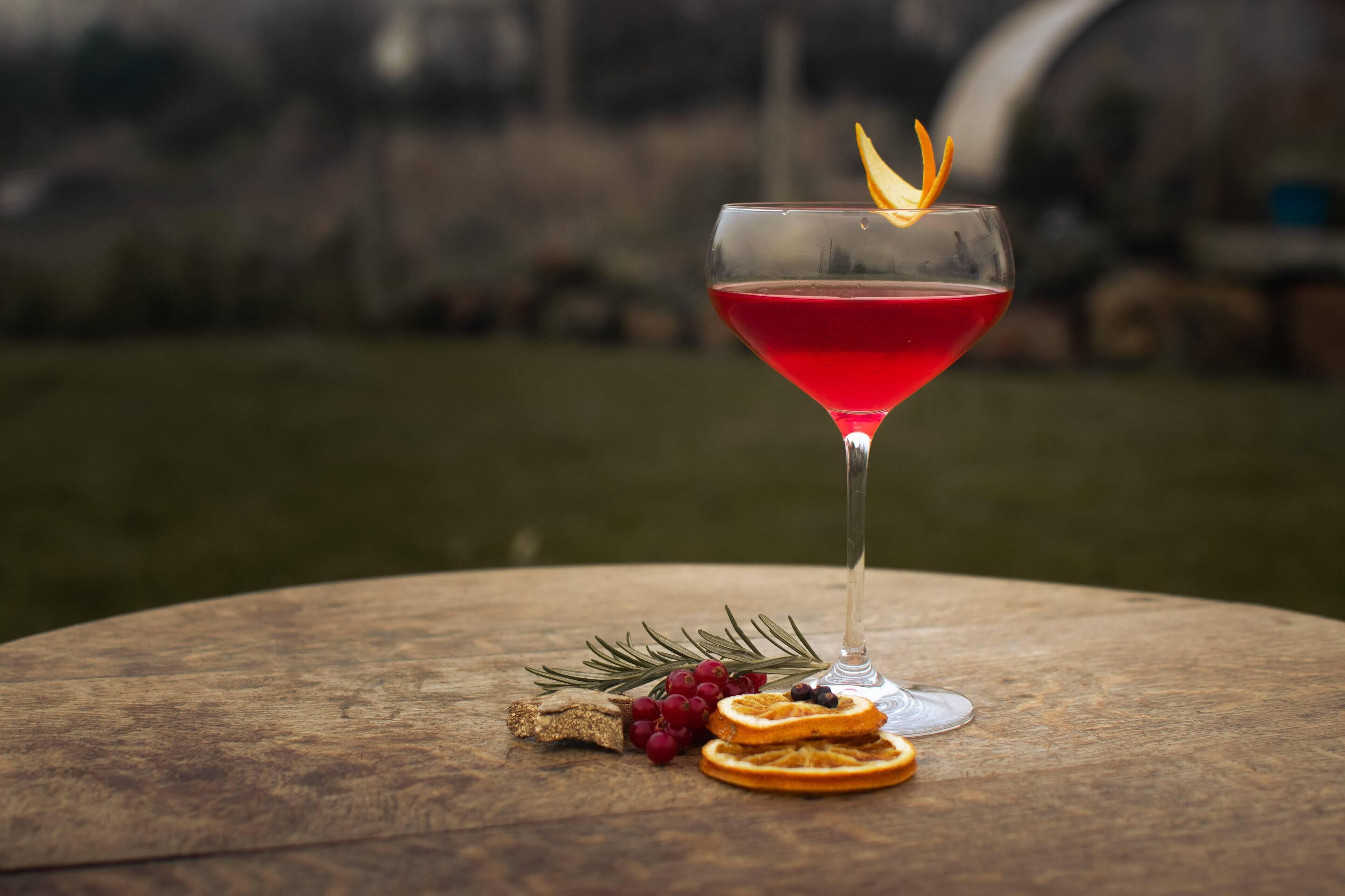 A martini glass with a red drink on a wooden table outdoors.