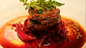 Un plato con un centro de carne, adornado con perejil, rodeado de verduras rojas y salsa.