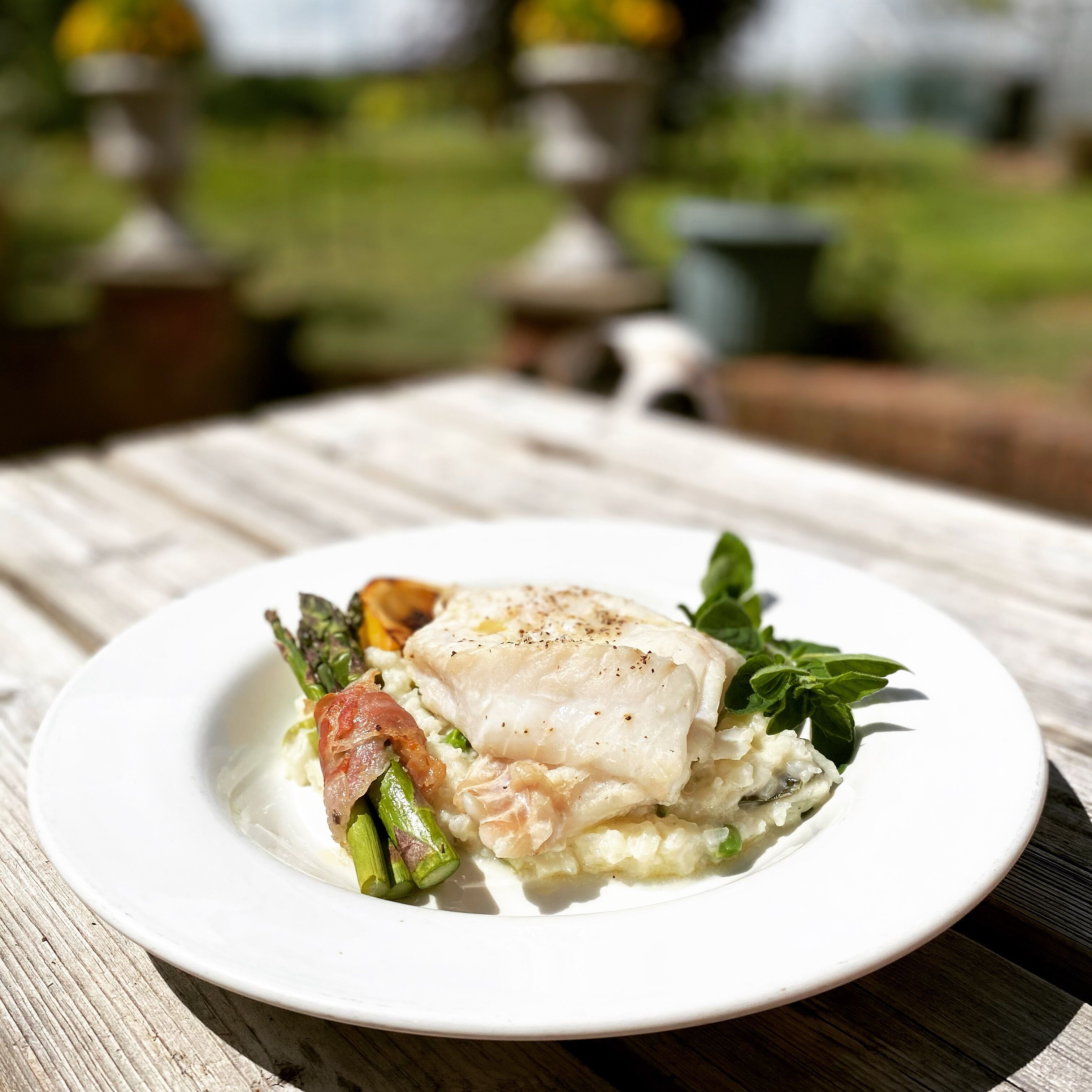 A white plate with a fish fillet, asparagus, and a garnish on a wooden table.