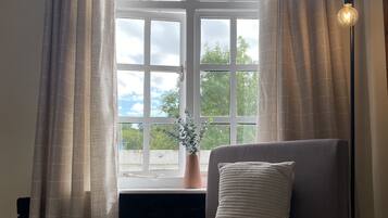 A bedroom with a bed, a window with curtains, a potted plant, and a floor lamp.