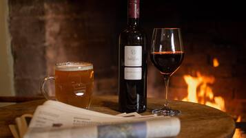 A bottle of wine, a glass of red wine, and a mug of beer on a wooden table with a newspaper underneath.