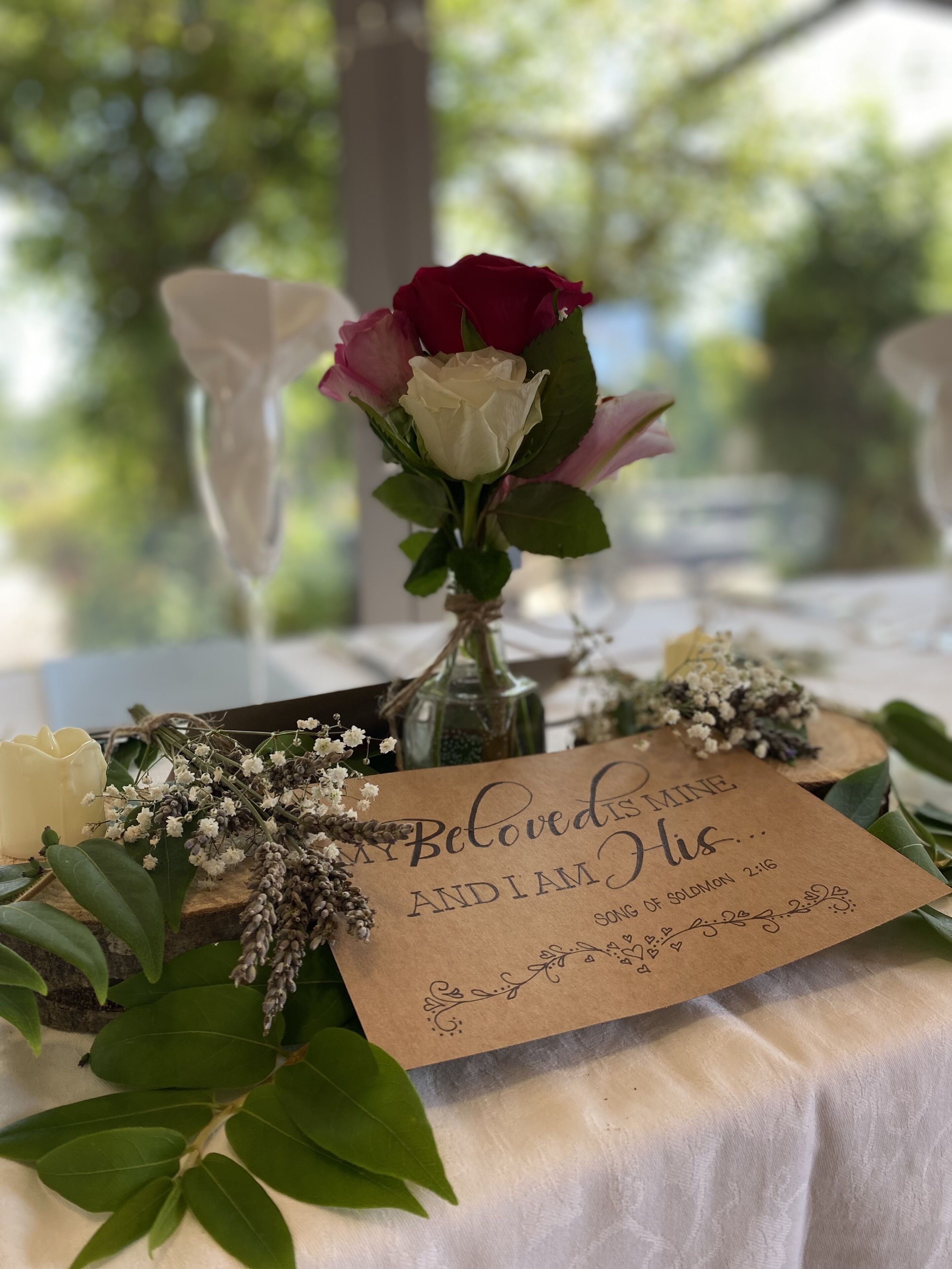 Une table ornée d’un bouquet de fleurs, d’une bougie et d’une carte avec un texte.
