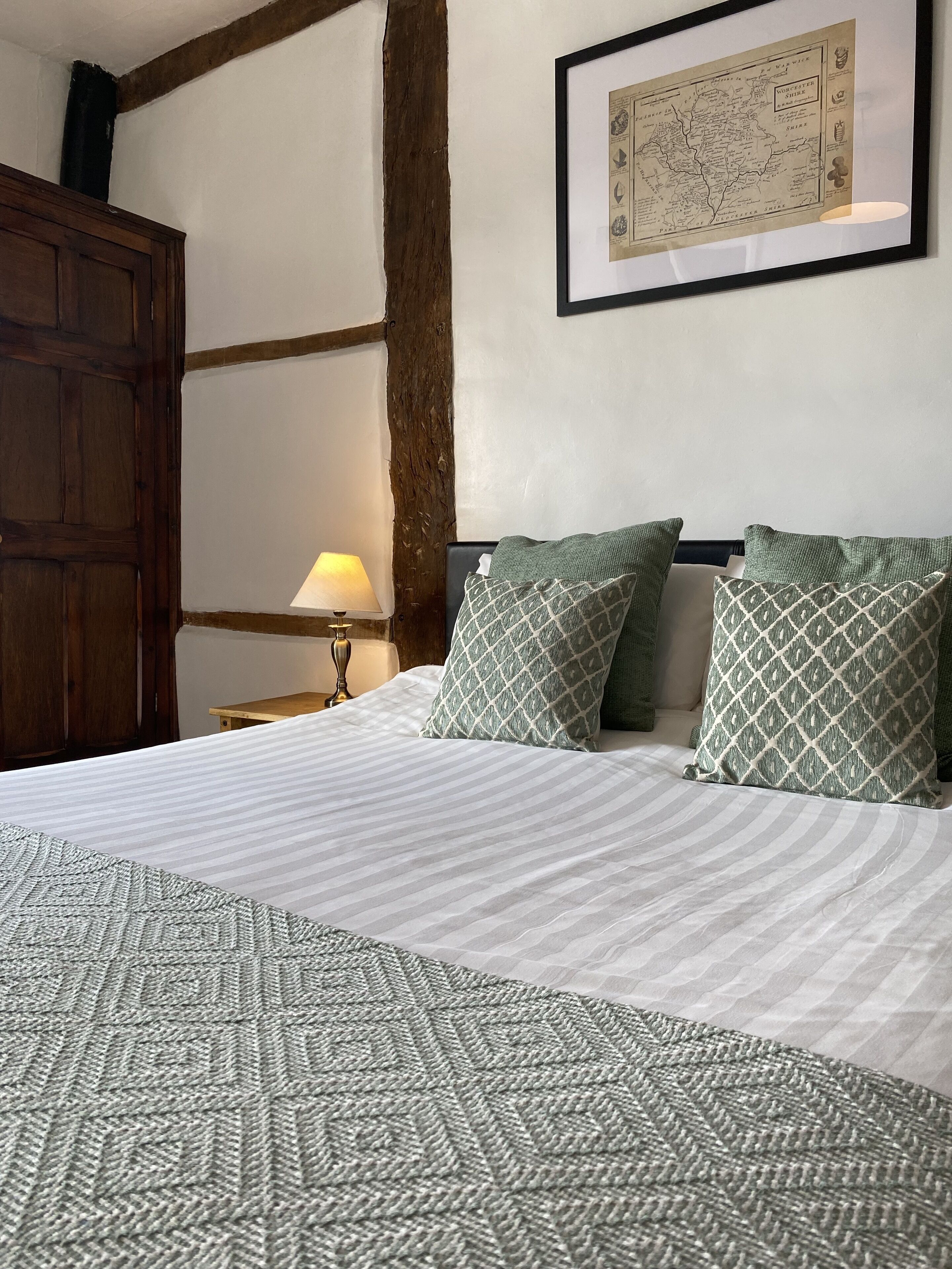 A neatly made bed with patterned bedding, a wooden headboard, a framed map on the wall, and a nightstand with a lamp.