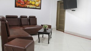 Un salon comprenant un canapé d’angle, une petite table sur laquelle est posé un vase de fleurs, et un téléviseur à écran plat fixé au mur.