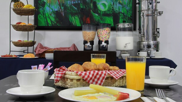 Une table dressée pour le petit-déjeuner, avec une machine à café, des corbeilles de fruits et une carafe de jus.
