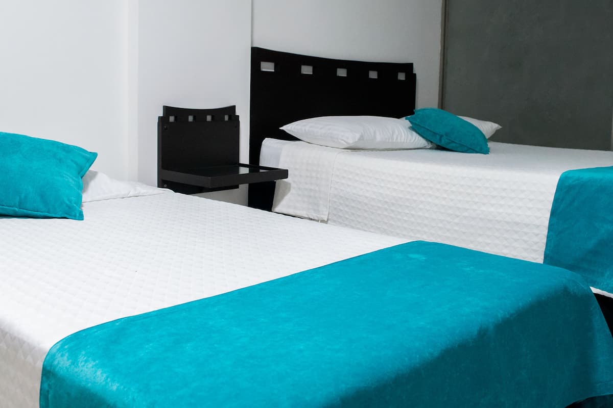 Two single beds with white bedding and teal accents, a black headboard, and a nightstand.