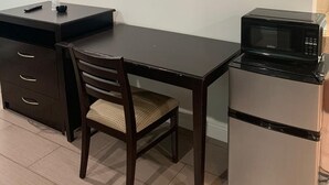 Eine kleine Küchenzeile mit Mikrowelle, Kühlschrank, einem Holzespeisetisch und einem an der Wand montierten Fernseher.