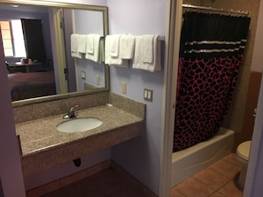 A bathroom with a granite sink, a mirror, a white towel, a black and red shower curtain, and a white toilet. - Budget Motel (Los Angeles)